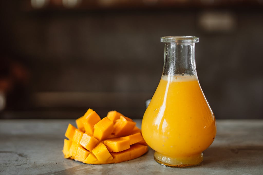 A refreshing and vibrant mango juice served in a clear glass bottle next to ripe mangos.