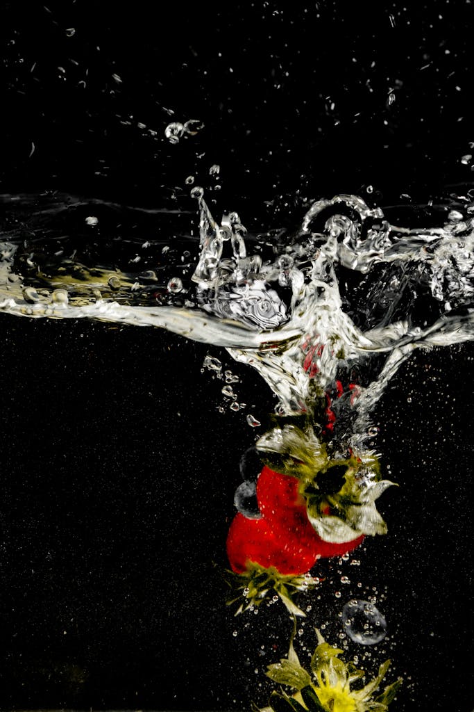 A vibrant strawberry plunges into clear water against a black background, creating an elegant splash effect.